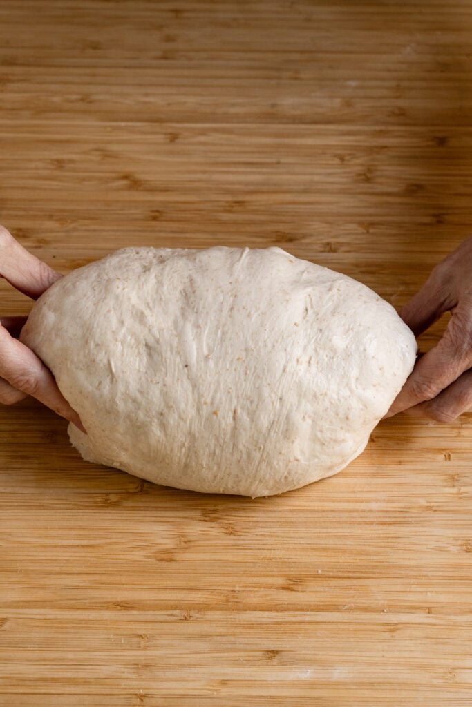 Hands pinching a boule shaped loaf od sourdough.