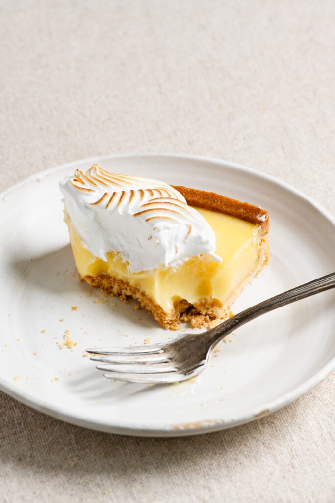 Partially eaten slice of lemon tart on a plate with a fork.