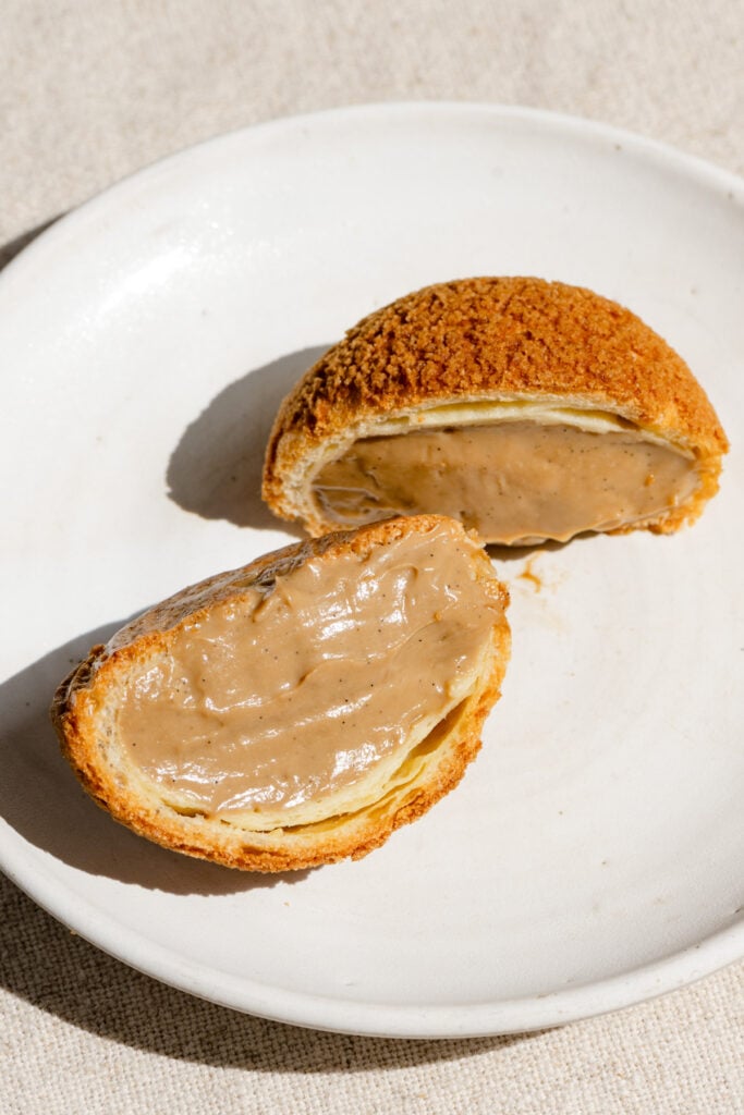 Choux au craquelin pastry filled with coffee pastry cream, cut in halof on a plate.