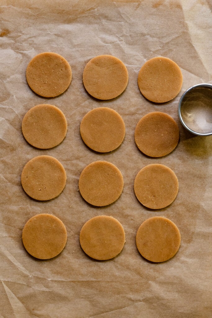 Overhead of craquelin dough discs on parchment paper next to a cookie cutter.