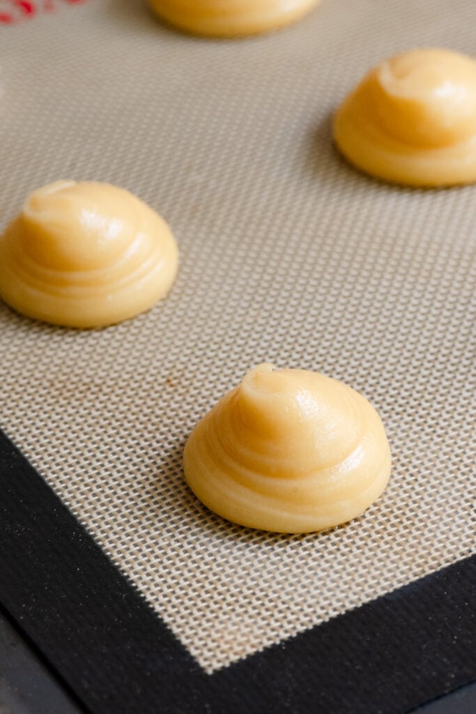 Pate a choux pastry piped into round mounds on a silicone mat.