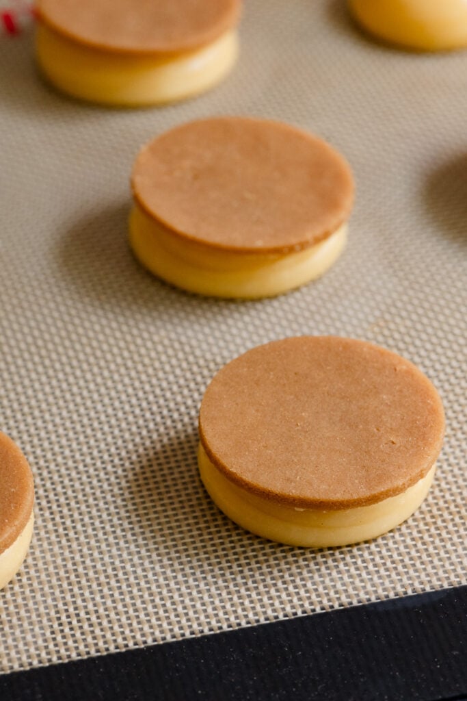 Choux pastry topped with frozen craquelin discs on a silicone mat.