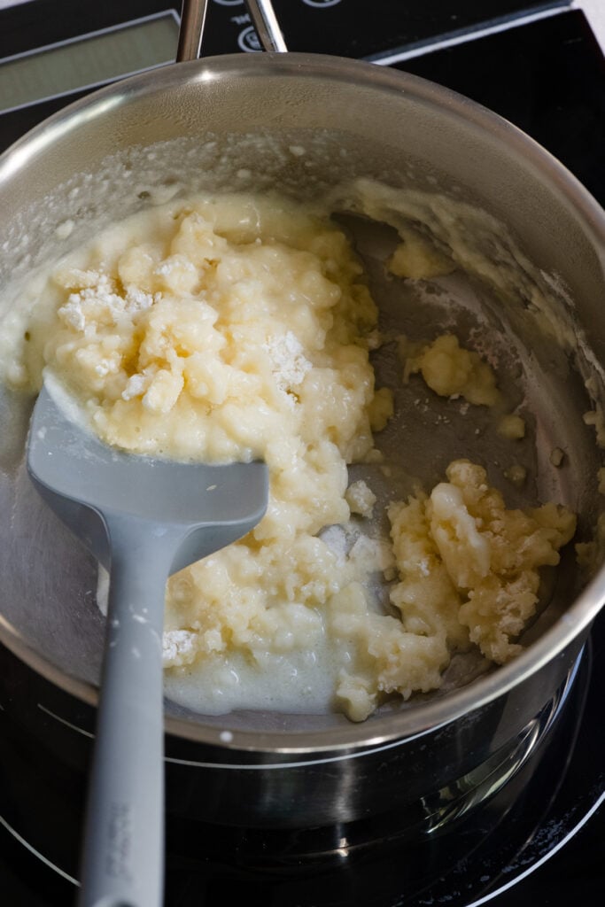 Flour being mixed into butter and milk in a saucepan.