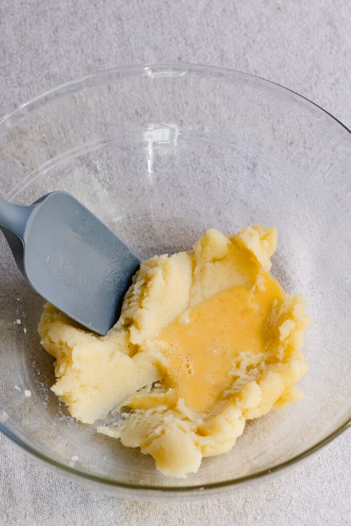 Beaten eggs being mixed into choux pastry dough inside a bowl.