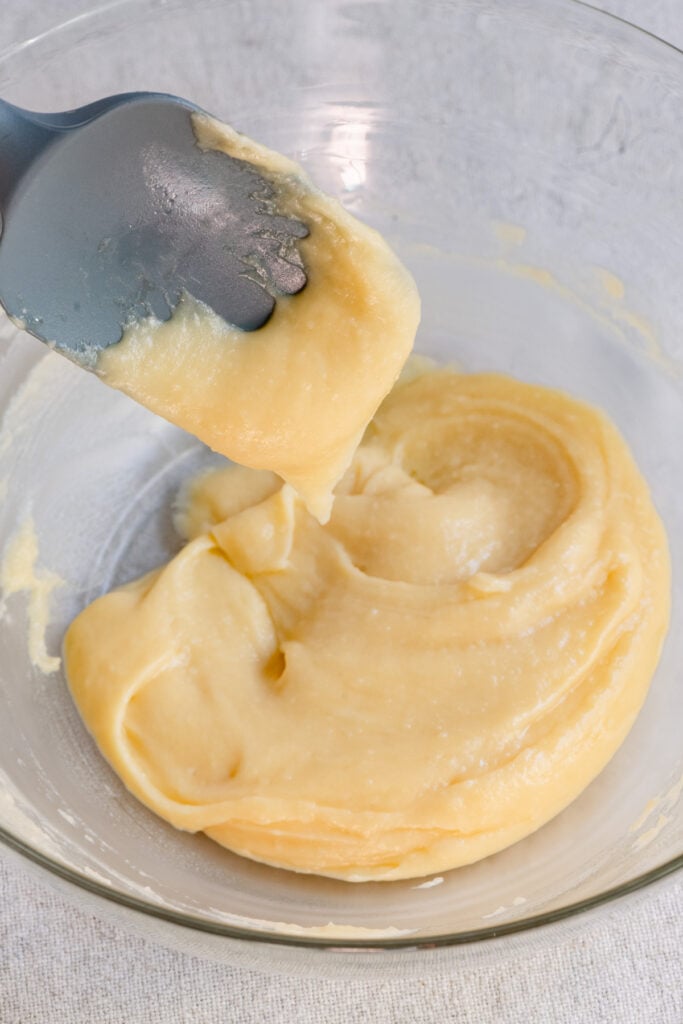 Choux pastry dough in a bowl being scooped by a spatula.