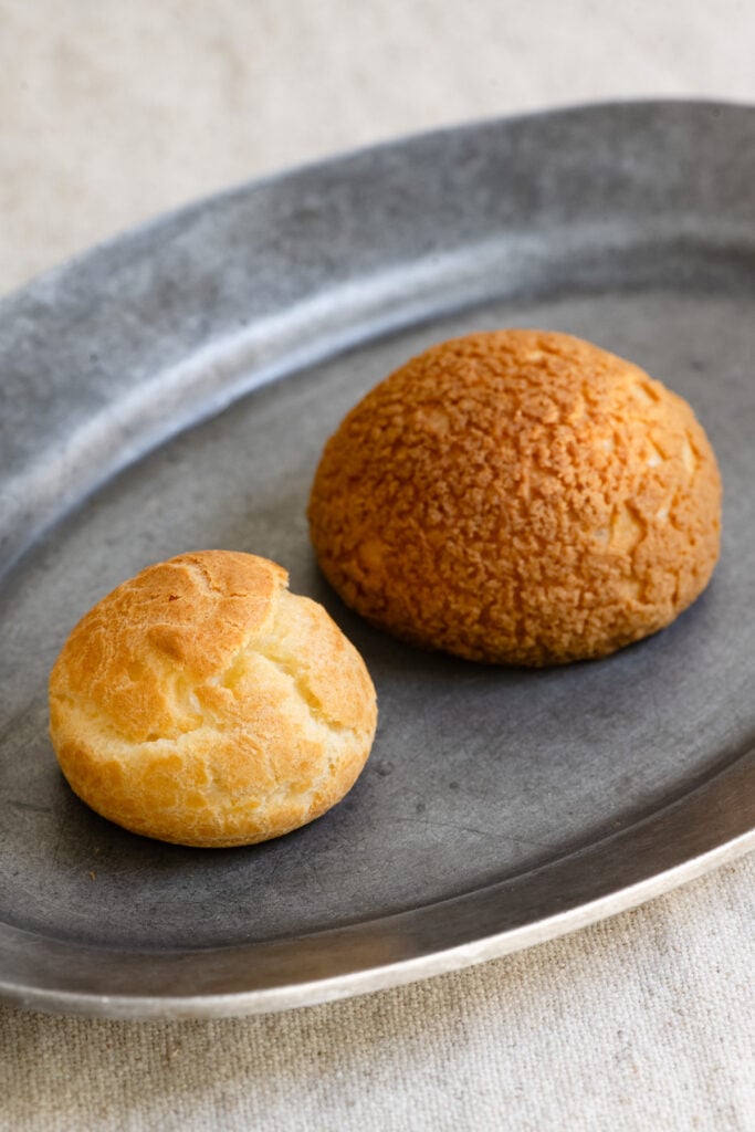 Plain choux pastry puff next to a choux au craquelin on a plate.
