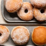 Sugar coated brioche donuts on trays next to a cup of coffee.