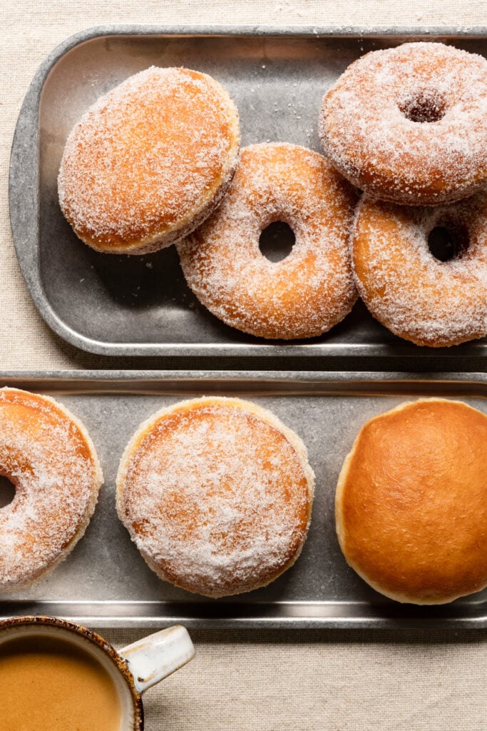 Sugar coated brioche donuts on trays next to a cup of coffee.