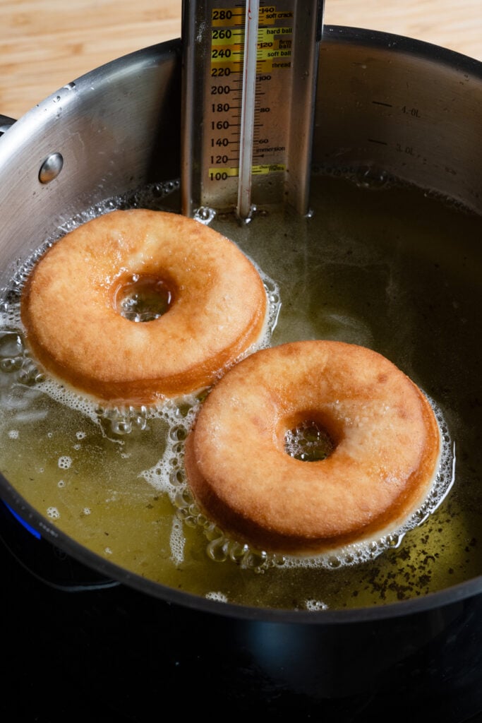 Two ring shaped donuts frying in a pot of oil.